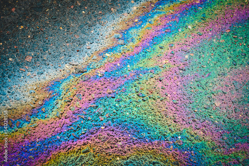 Puddles are contaminated with multicolored streams of oil. Oil stains on wet asphalt.