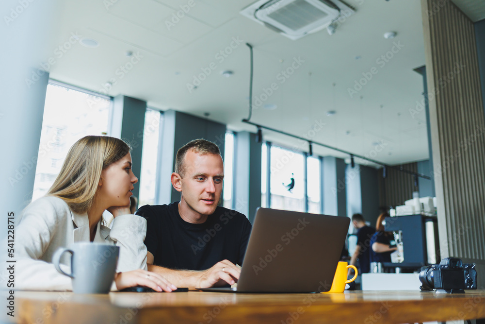 Positive young colleagues managers sitting at the table and laughing looking at the laptop. Teamwork concept. Selective focus. Modern successful people Positive young colleagues managers sitting at the table and laughing looking at the laptop. Teamwork concept. Selective focus. Modern successful people