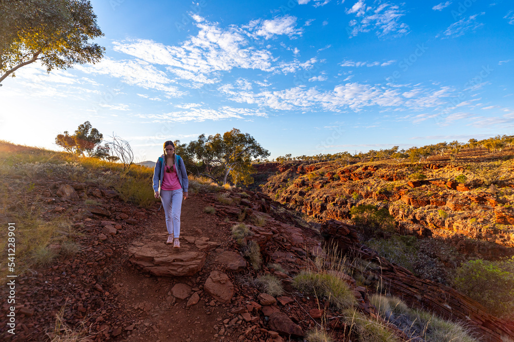 Backpacker girl hiking in karijini national park, australia at sunrise; sunrise in the red desert in the australian outback