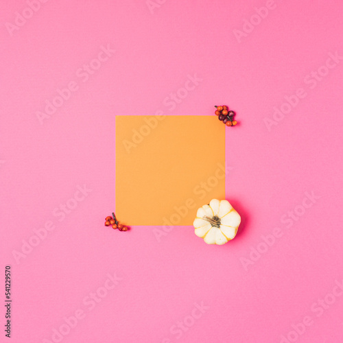 Vibrant autumn minimal flat lay yellow greeting note on vibrant pink background. Fall or Thanksgiving concept decorated with pumpkin. Creative colorful October season.