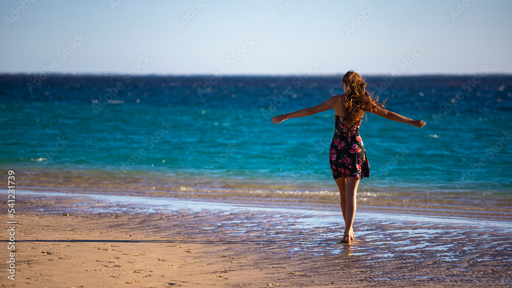long-haired girl in black dress dances on beach in coral bay, australia at sunset, romantic sunset walk on beach in western australia