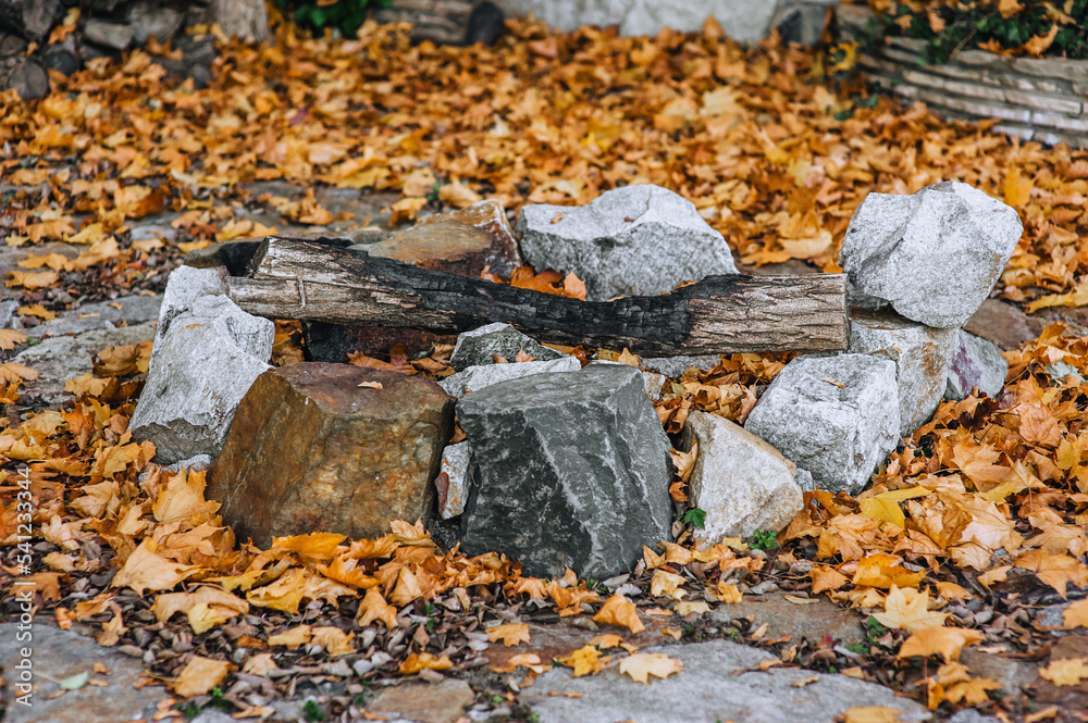 Homemade fireplace made of stones and extinct firewood in nature in autumn with fallen yellow maple leaves. Photography of nature.