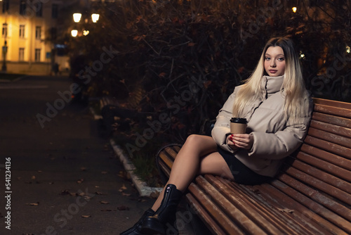 A young girl drinks coffee while sitting on a bench.