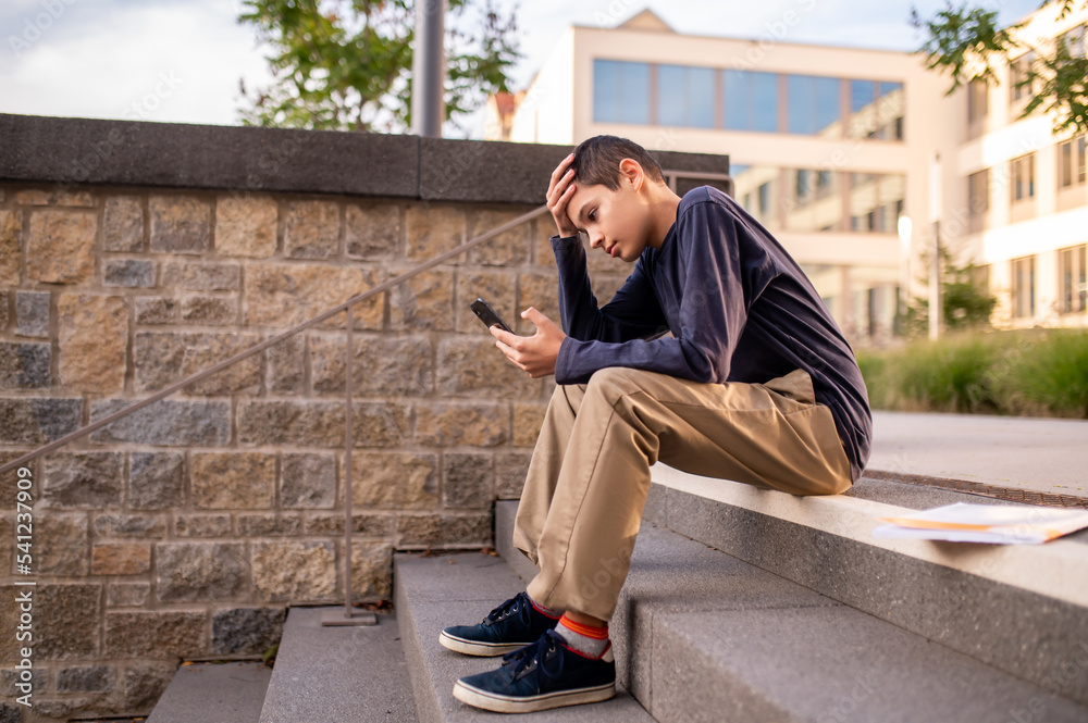 Upset adolescent reading bad news on his smartphone Upset adolescent reading bad news on his smartphone