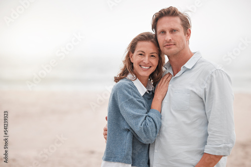 Happy, couple and portrait smile on a beach together relaxing while enjoying quality bonding time in the outdoors. Man and woman smiling in happiness for hug, relationship love or care on sandy ocean