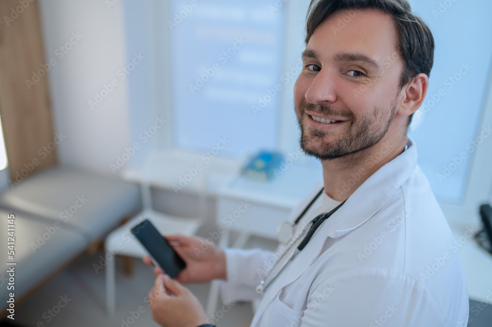 Joyous doctor with the cell phone seated in his office