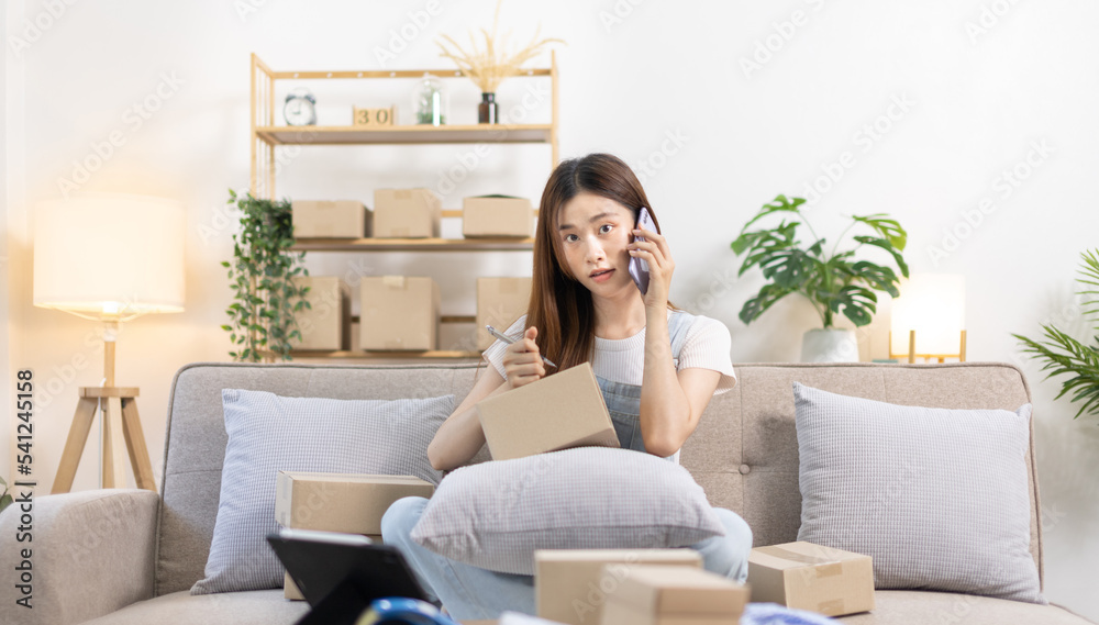 E-commerce businessman is talking on the phone with a customer who comes in to inquire and place her order, Woman writes mailbox address in preparation for delivery, SME entrepreneur, Packing box. E-commerce businessman is talking on the phone with a customer who comes in to inquire and place her order, Woman writes mailbox address in preparation for delivery, SME entrepreneur, Packing box.