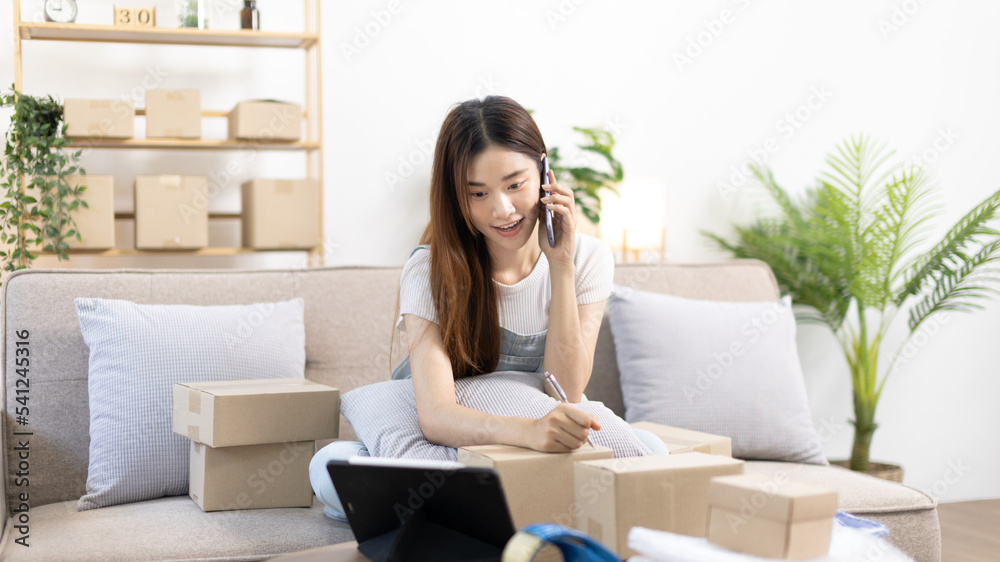 E-commerce businessman is talking on the phone with a customer who comes in to inquire and place her order, Woman writes mailbox address in preparation for delivery, SME entrepreneur, Packing box. E-commerce businessman is talking on the phone with a customer who comes in to inquire and place her order, Woman writes mailbox address in preparation for delivery, SME entrepreneur, Packing box.