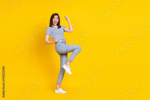 Photo of satisfied overjoyed lady raise arm leg rejoice yeap stand empty space isolated on yellow color background