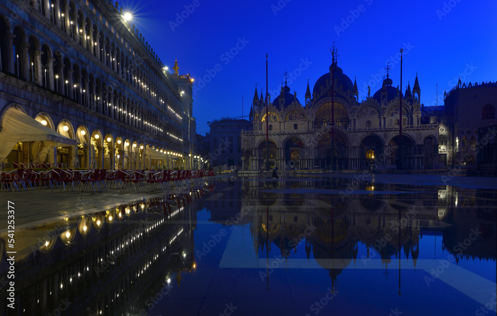 Fototapeta premium Der Markusplatz in Venedig zur Blauen Stunde am frühen Morgen und im nächtlichen Hochwasser spiegelt sich der Markusdom