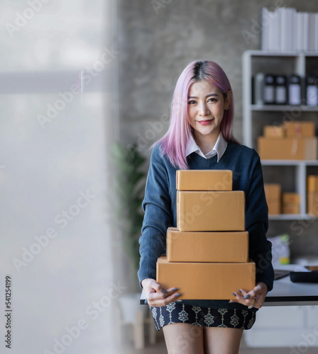 Startup SME small business entrepreneur of freelance Asian woman using a laptop with box Cheerful success Asian woman her hand lifts up online marketing packaging box and delivery SME idea concept © David