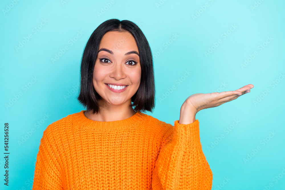 Photo of satisfied lovely girl with bob hairdo dressed orange pullover palm demonstrating object isolated on turquoise color background Photo of satisfied lovely girl with bob hairdo dressed orange pullover palm demonstrating object isolated on turquoise color background