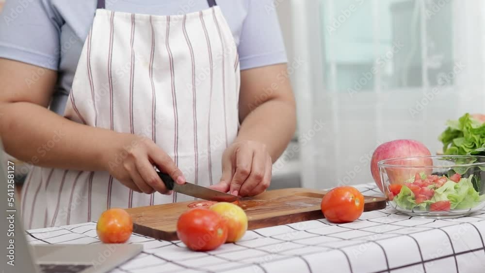 Fat Asian woman cooking in kitchen and chopping fresh organic vegetables on chopping board. Learn to make salads and healthy food from social media. health care concept Eat healthy food to lose weight Fat Asian woman cooking in kitchen and chopping fresh organic vegetables on chopping board. Learn to make salads and healthy food from social media. health care concept Eat healthy food to lose weight