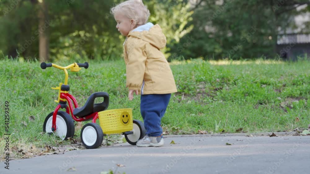 Happy kid having fun learning to ride tricycle for toddlers outdoors, 1.5 year old child playing with red yellow tricycle for younger kids in the park Happy kid having fun learning to ride tricycle for toddlers outdoors, 1.5 year old child playing with red yellow tricycle for younger kids in the park