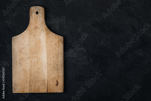 Wooden cutting board on dark stone concrete background, top view.
