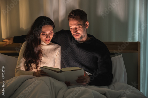 Caucasian couple sitting on their bed under blanket in dark room watching laptop screen.