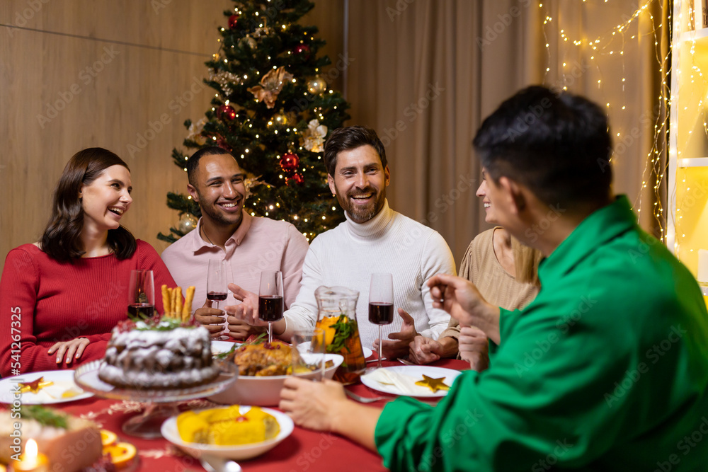 Friends celebrate Christmas eve or New Year holiday paty together sitting at the table. Feast at home group of multi ethnic festive christmas dinner. happy cheerful people clink wine glasses laugh