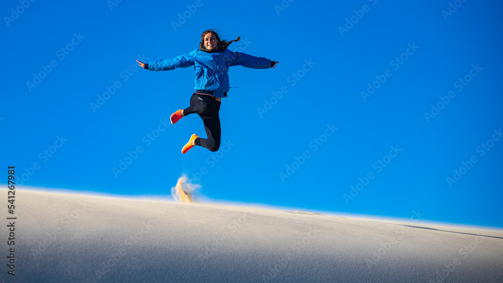 A happy girl jumps for joy while walking on a huge sand dune in coral bay western australia; walking on a sand desert in the australian outback