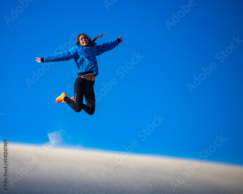 A happy girl jumps for joy while walking on a huge sand dune in coral bay western australia; walking on a sand desert in the australian outback
