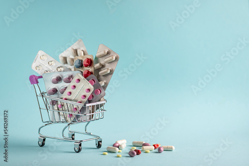Many medicine pills, tablets and vitamins in a small supermarket shopping cart on a blue  background, pharmaceutical picture taken with soft focus Pharmacy theme, capsular tablets 
