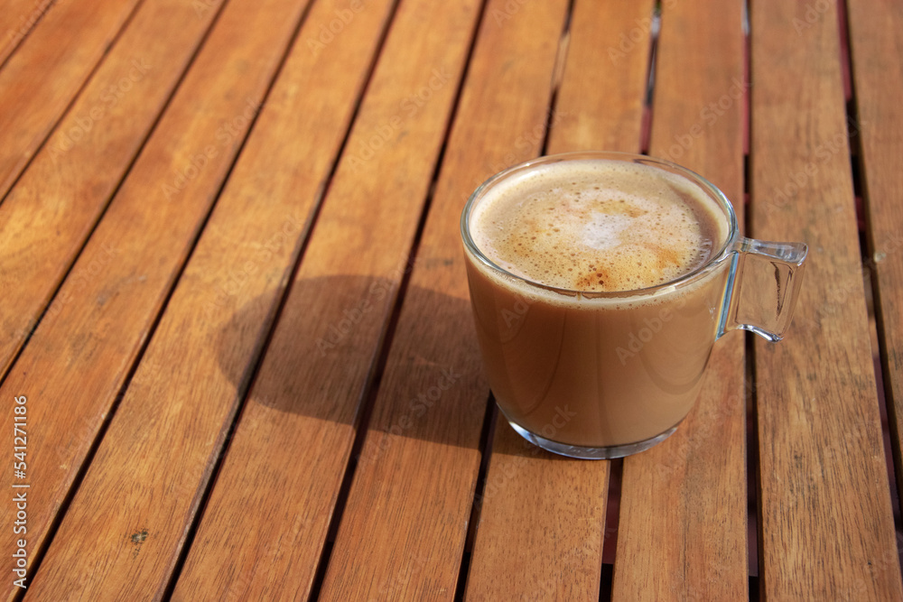 Fresh coffee on a wooden table during breakfast. The sun falls on the cup. Time to relax