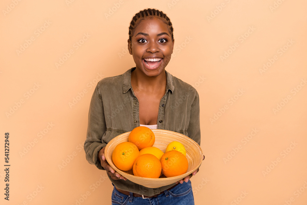 Portrait of funky crazy girl arms hold oranges bowl toothy smile isolated on beige color background Portrait of funky crazy girl arms hold oranges bowl toothy smile isolated on beige color background