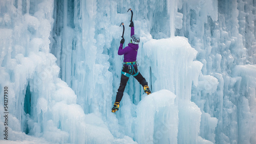 Alpinist woman with ice climbing equipment on a frozen waterfall