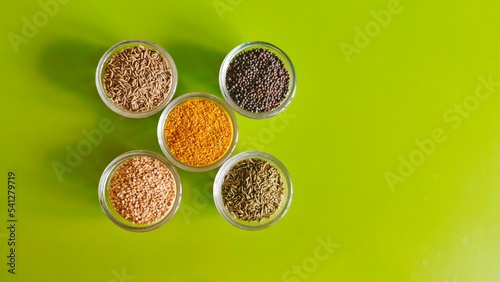 Five varieties of seeds displayed in separate bowls—middle one contains rai dal (split and skinned mustard seeds), top left cumins, top right black mustard, bottom left sesame, bottom right fennel photo