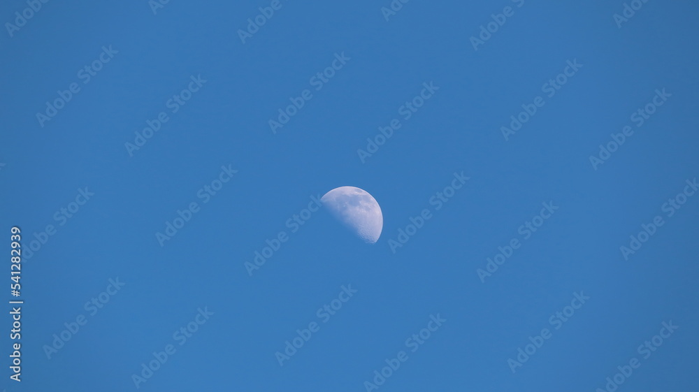 The moon shining in the daytime against the blue sky The moon shining in the daytime against the blue sky