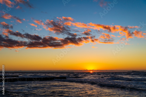 Orange clouds sunset sky above waves Baltic sea. Magic hour.