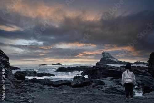 Girl standing in front of the ocean at sunset