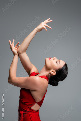 Side view of brunette woman in red dress dancing tango isolated on grey