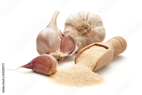 Ground dried garlic on a wooden spatula surrounded by whole heads of garlic