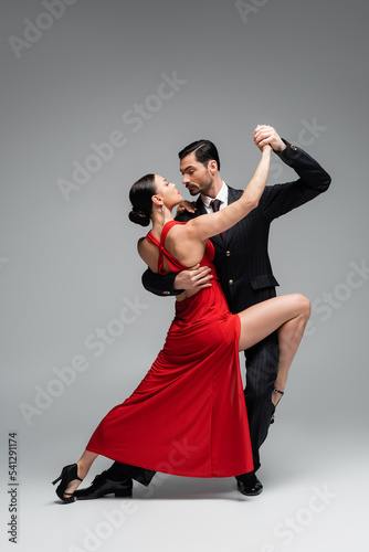 Full length of elegant couple dancing tango on grey background photo