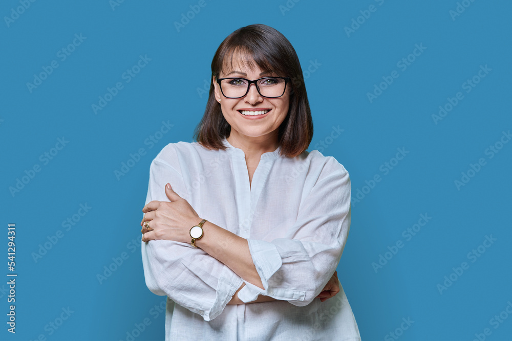 Positive middle aged woman looking at camera on blue studio background Positive middle aged woman looking at camera on blue studio background