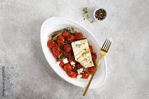 Dish with baked cherry tomatoes, feta cheese drizzled with salt, olive oil, garlic and thyme. Top view, copy space. photo