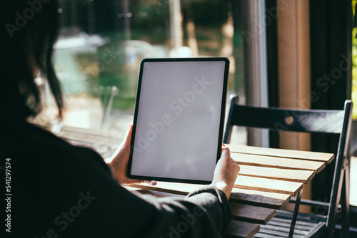 Woman with red nails holding an iPad in a bright room on a wooden table near the window. Work from home