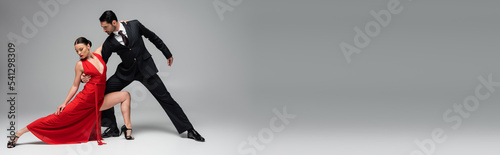 Stylish man in suit performing tango with woman on grey background, banner photo