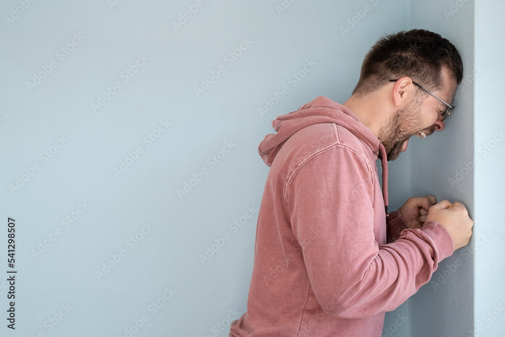 Man in stress and anger, he leaned his forehead against the wall and screams loudly. Copy space. Man in stress and anger, he leaned his forehead against the wall and screams loudly. Copy space.