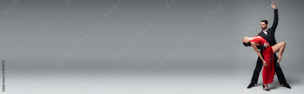 Professional ballroom dancer posing while dancing tango with partner on grey background, banner