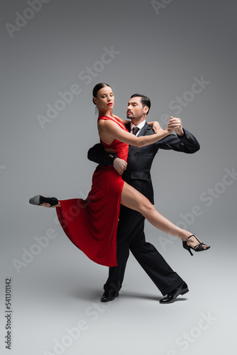 Stylish woman in red dress dancing tango with man on grey background