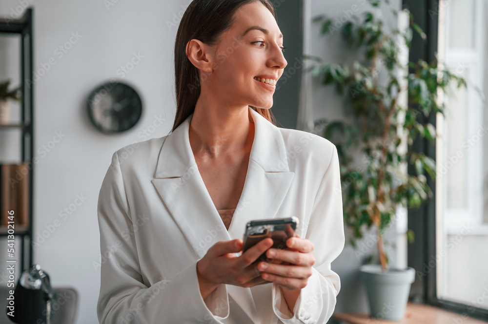 Using smartphone. Young beautiful woman in formal clothes is working at office