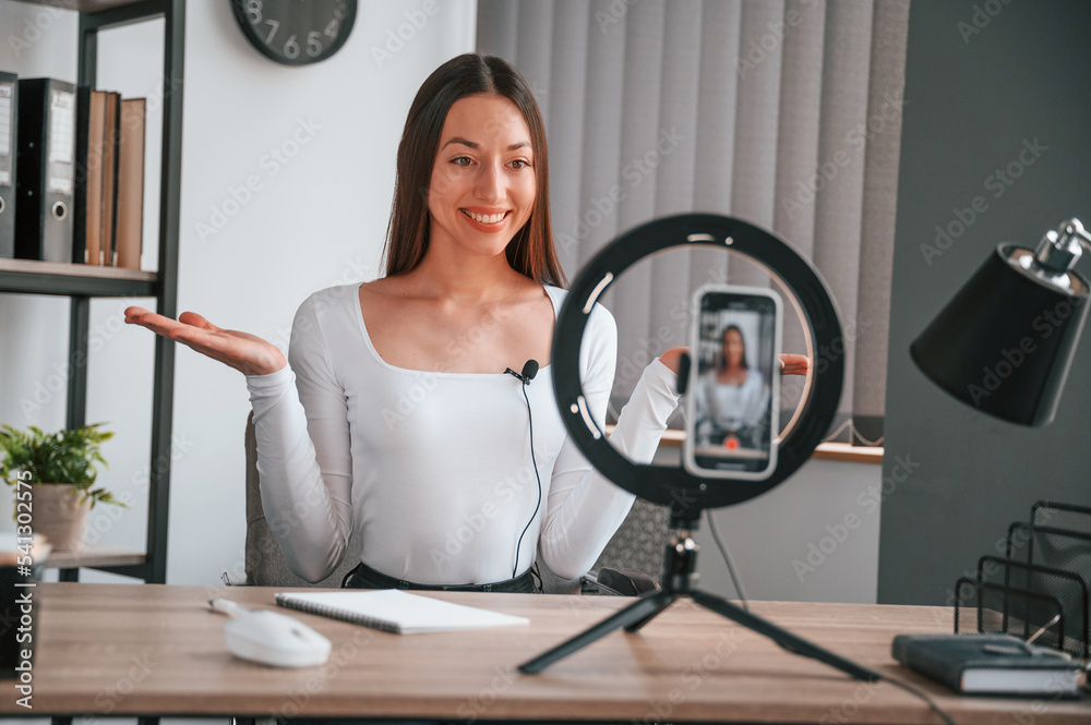 Talking, doing online master class. Young beautiful woman in white clothes is in the office Talking, doing online master class. Young beautiful woman in white clothes is in the office