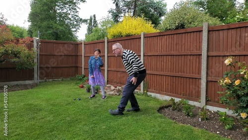 Caucasian Granddaughter and Grandfather playing in backyard garden a game of petanque, Colchester, Essex