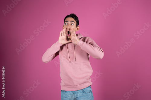 Emotional young man in a pink sweater on a pink background. Gestures by male hands.