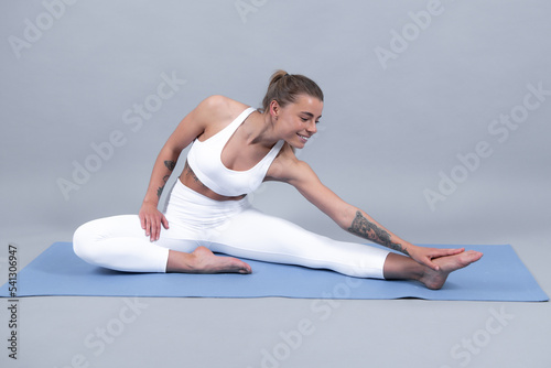 Young sporty woman in sportswear practicing fitness on mat, beautiful girl doing exercise, working out on gray studio background.