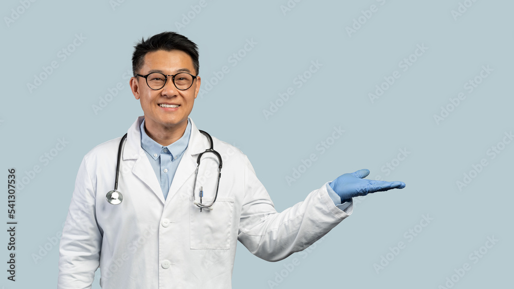 Cheerful middle aged chinese man doctor in white coat, protective gloves, goggles shows hand with empty space Cheerful middle aged chinese man doctor in white coat, protective gloves, goggles shows hand with empty space