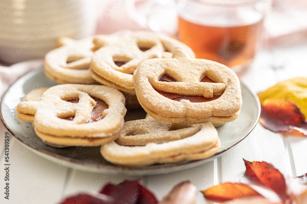 Linzer cookies in the shape of a Halloween pumpkin on white table.