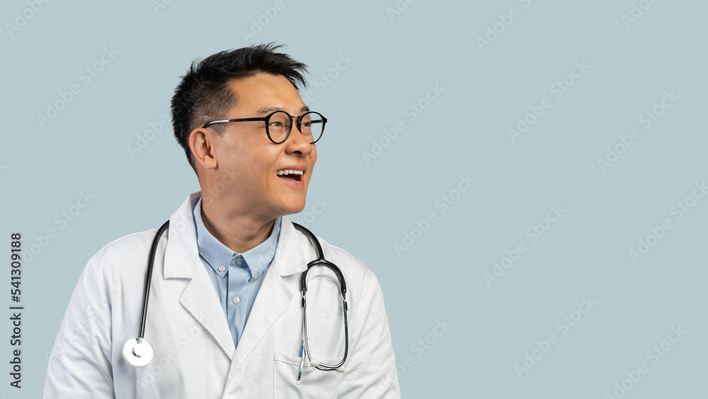 Smiling surprised middle aged chinese man doctor in white coat, glasses looks at empty space Smiling surprised middle aged chinese man doctor in white coat, glasses looks at empty space