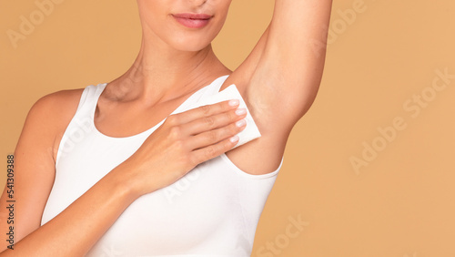 Hyperhidrosis concept. Closeup of young lady wiping her under arm area with napkin towel, standing on beige background